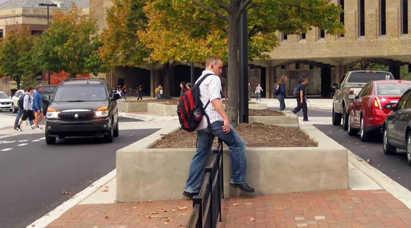 Pedestrian stepping over a short fence in a broad traffic median