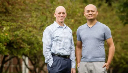2 people standing together with a green landscape behind them