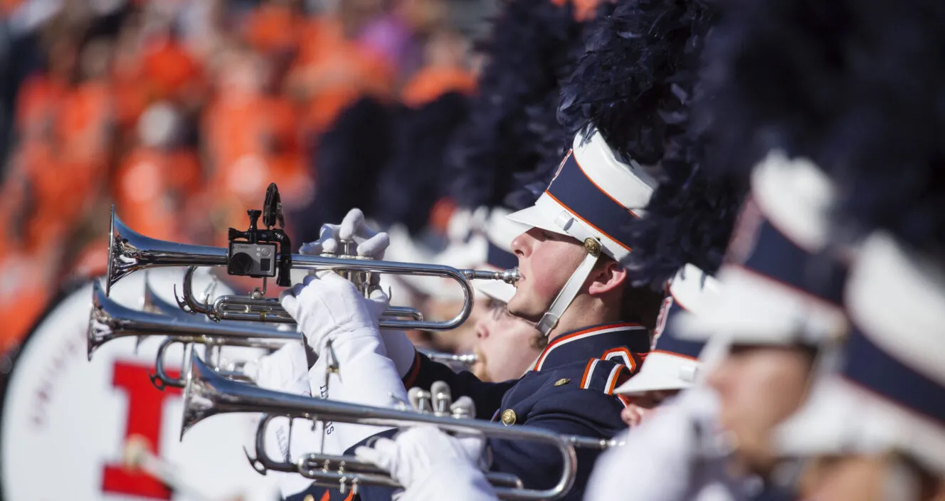 Uniformed members of marching band, playing trumpets.