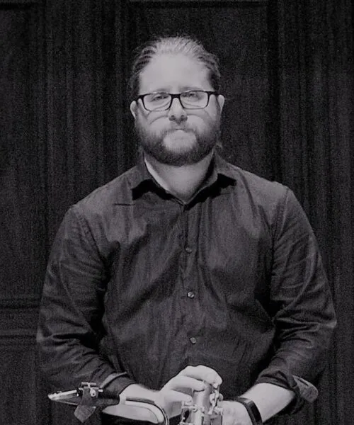 Operations Manager, Nathan Mandel, in black and white photo holding a baritone saxophone