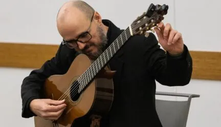 Dr. Guido Sánchez Portuguez, assistant professor in FAA, tunes his acoustic guitar during his concert performance at the Champaign Public Library on Jan. 30.  Photo by Sarah Slattery, The Daily Illini
