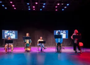actors on a stage with music stands and screen projections