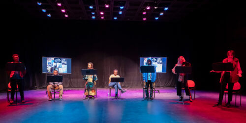 actors on a stage with music stands and screen projections