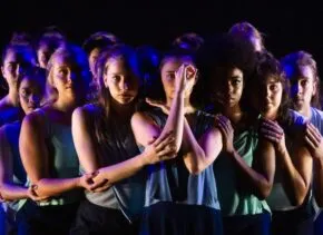 many dancers gatherd in dark blue lighting in embrace