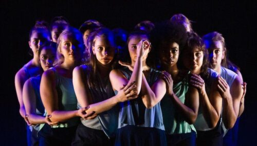 many dancers gatherd in dark blue lighting in embrace