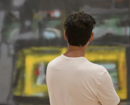 Person from behind looking at a painting with grays, greens, and yellows