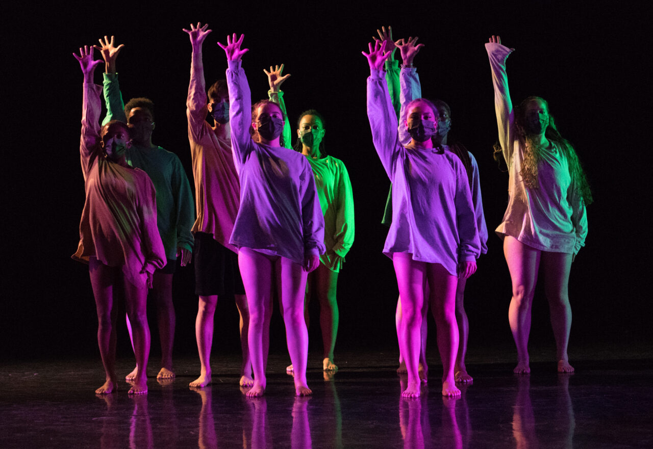 Dancers with one arm up under neon lights from Merrylynns Prayer choreographed by Kennedy Cowan, Senior Concert 2022. Photo by Natalie Fiol.