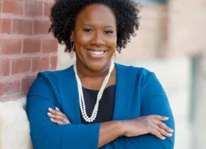 Mariam Thiam standing against brick wall with arms crossed