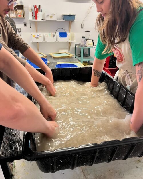 students with hands in papermaking water