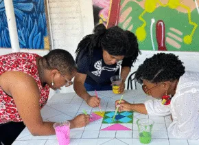 3 artists lean over table painting together