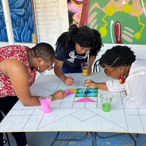 3 artists lean over table painting together