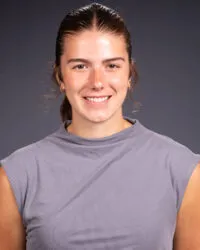 Headshot image of a person wearing a grey short-sleeve t-shirt in-front of a dark background.