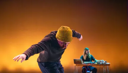 person bent over with arms outstretched, musician in background playing