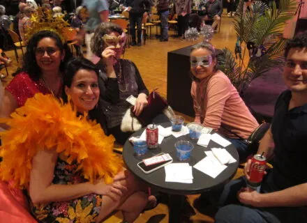 people dressed in bright colors and masks sit around a table smiling
