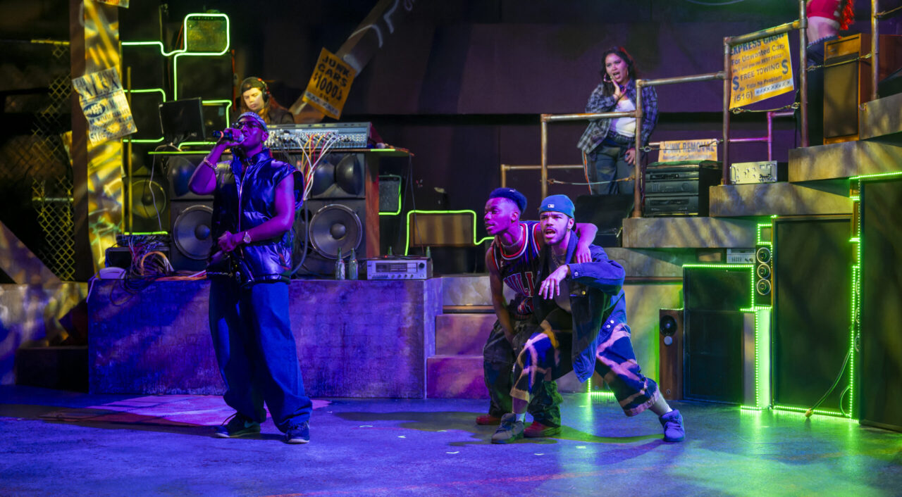 people sing and rap on a tiered stage with neon lighting