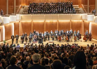 many people performing onstage in a concert hall orchestra with full audience watching