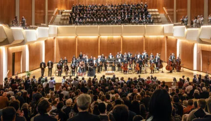 many people performing onstage in a concert hall orchestra with full audience watching