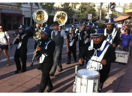 a marching band with people playing drums and horns marches down the street