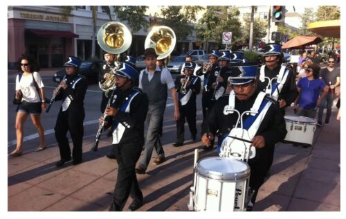 a marching band with people playing drums and horns marches down the street