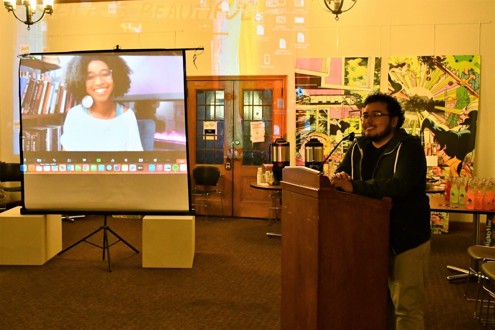 someone talking into a mic at a podium and a screen with a smiling Gumbs