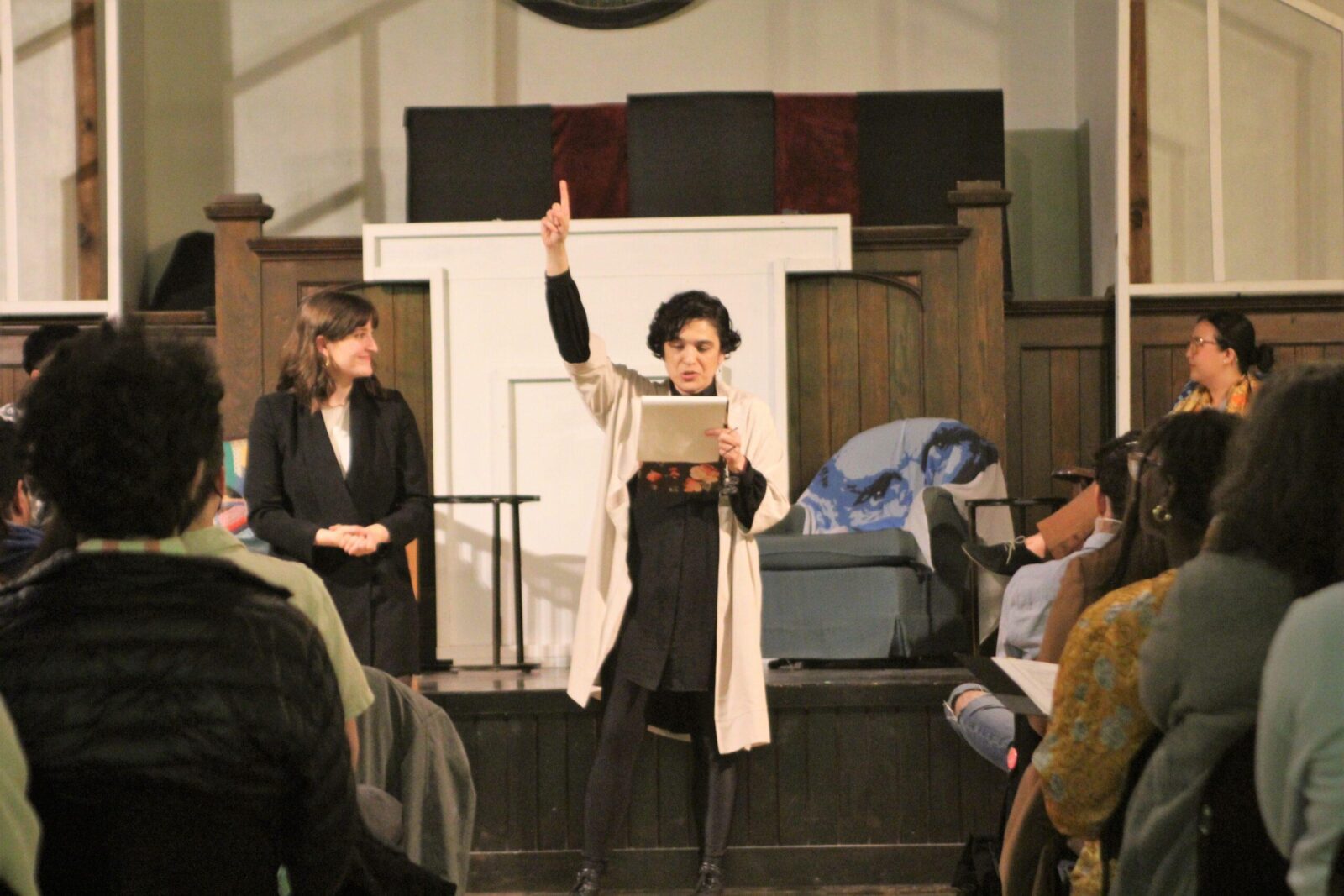 sandra ruiz standing in front of stage with one finger up while reading from notebook