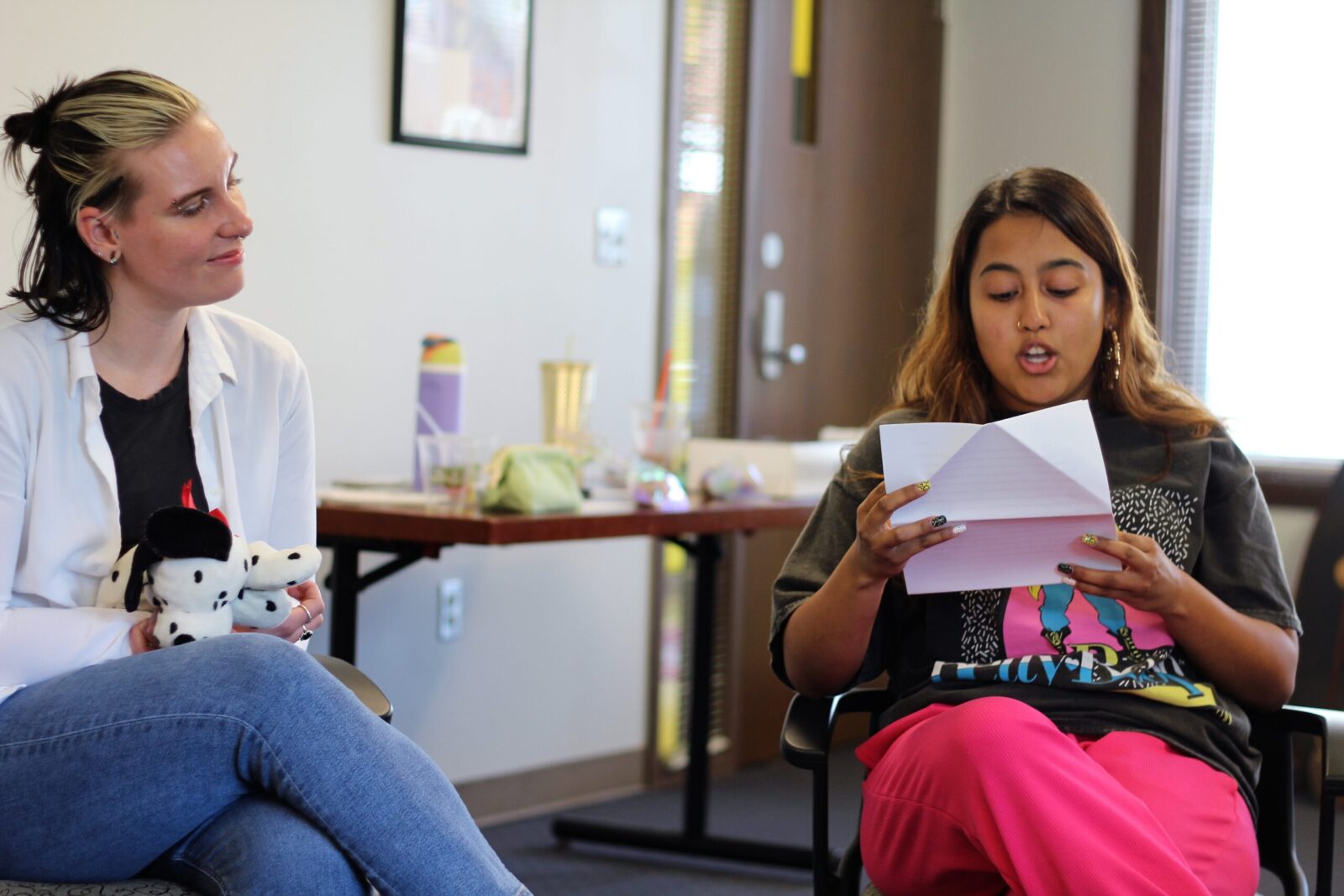 two people sitting, one person reads a letter the other person watches