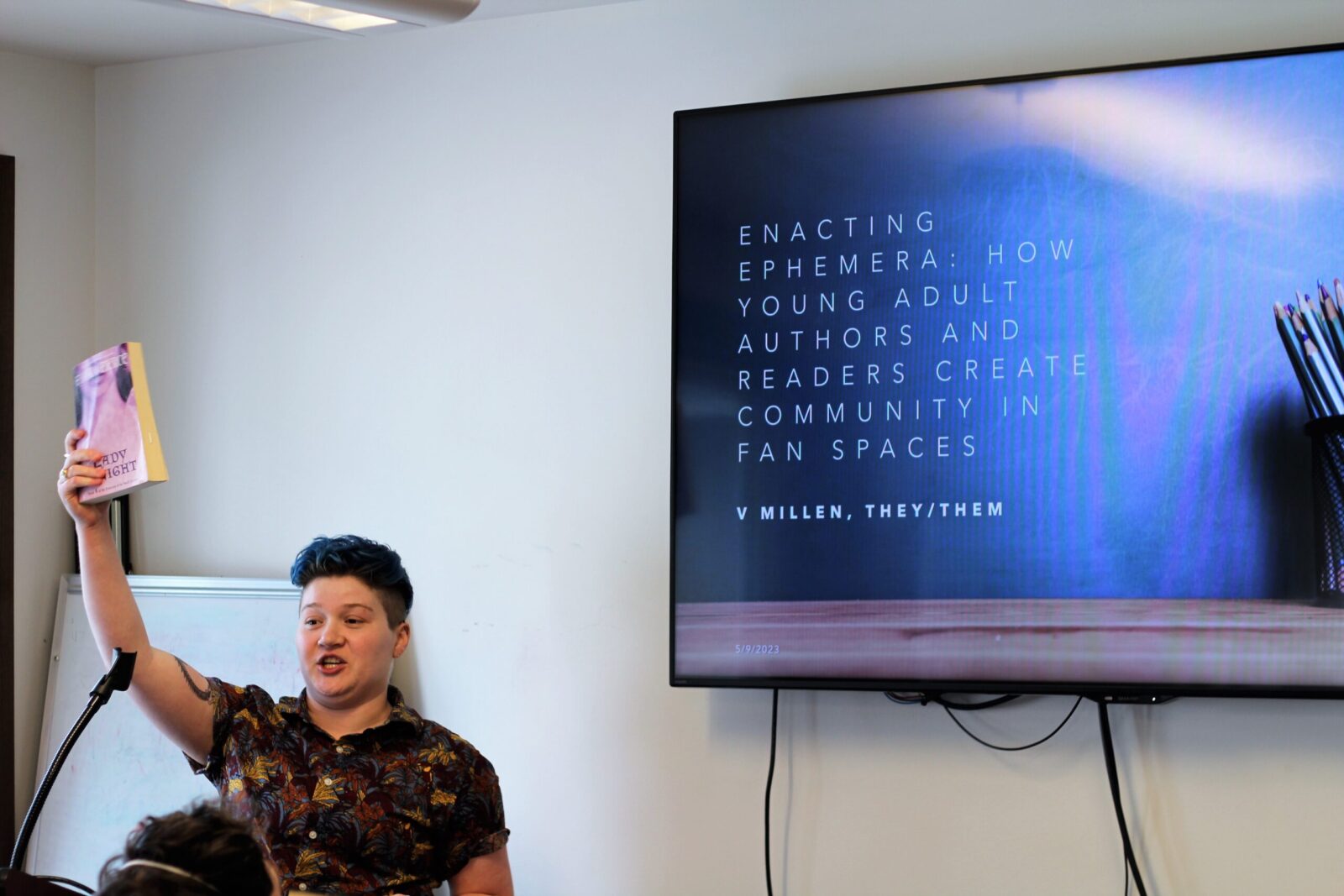 a person holds up a book with a presentation slide up behind them