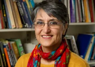 Photo of Dr. Miraftab in front of a bookshelf wearing a yellow sweater with a red scarf