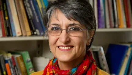 Photo of Dr. Miraftab in front of a bookshelf wearing a yellow sweater with a red scarf