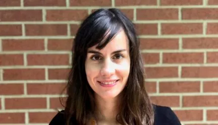 a person with long brown hair and a navy blue shirt looks at camera while smiling