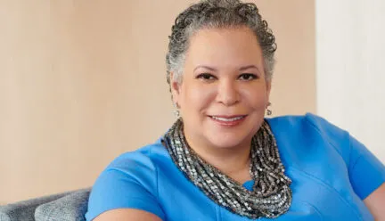 Photo of Dr. Edwards sitting on a chair with a blue blouse against a beige wall