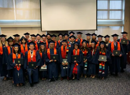 Group photo of graduates in their orange and blue regalia