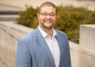 Photo of Dr. Andrew Greenlee outside in front of a concrete walkway in blue sports coat