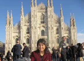 Photo of Colleen in front of a large cathedral feeding pigeons