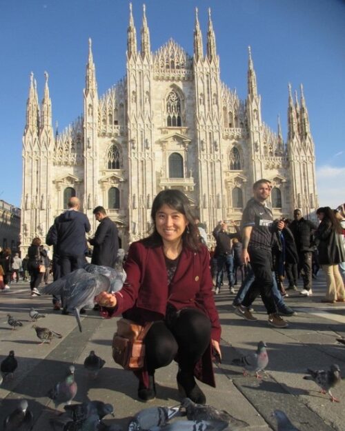 Photo of Colleen in front of a large cathedral feeding pigeons