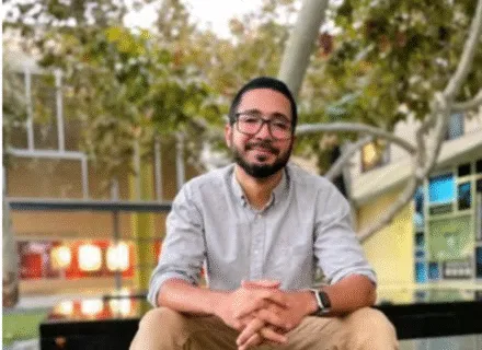 Photo of Omar sitting on a bench outside in front of a tree