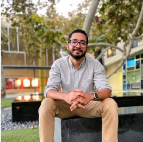 Photo of Omar sitting on a bench outside in front of a tree