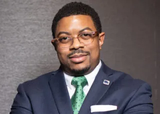 Photo of Jon Petty in a blue suit in front of a gray wall