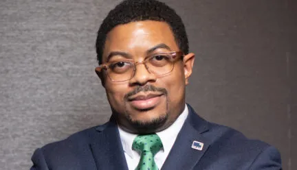 Photo of Jon Petty in a blue suit in front of a gray wall