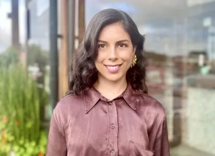 Photo of Camila in rose-colored silk blouse in front of a window