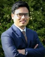 Photo of Shuvangkor Shusmoy Roy in front of tree wearing blue suit