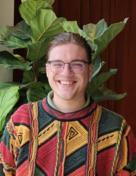 Photo of Brandon Snyder in colorful sweater in front of a green plant and orange curtain