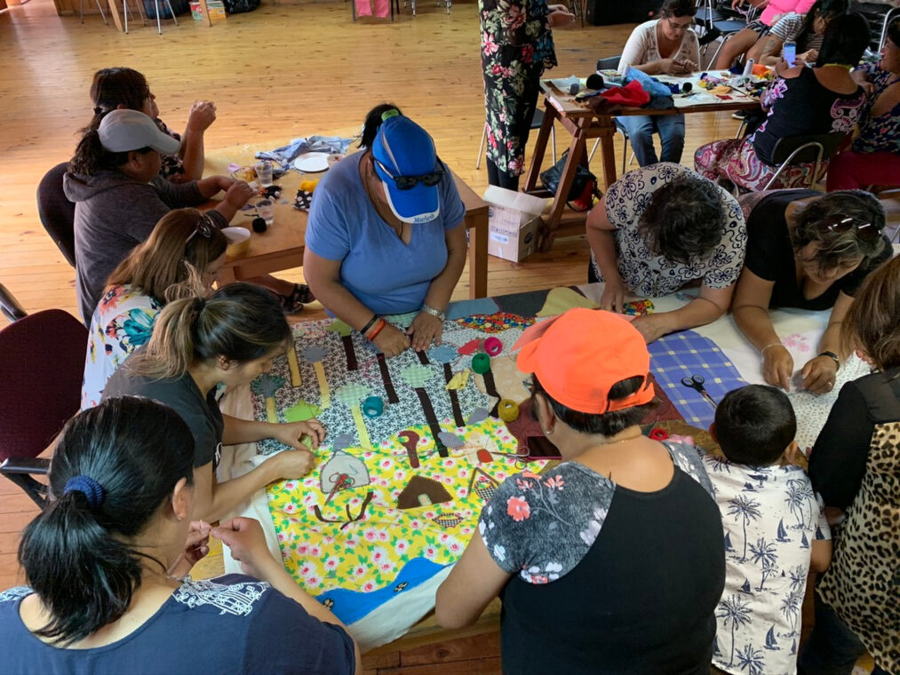several people gathered around a table sewing a textile