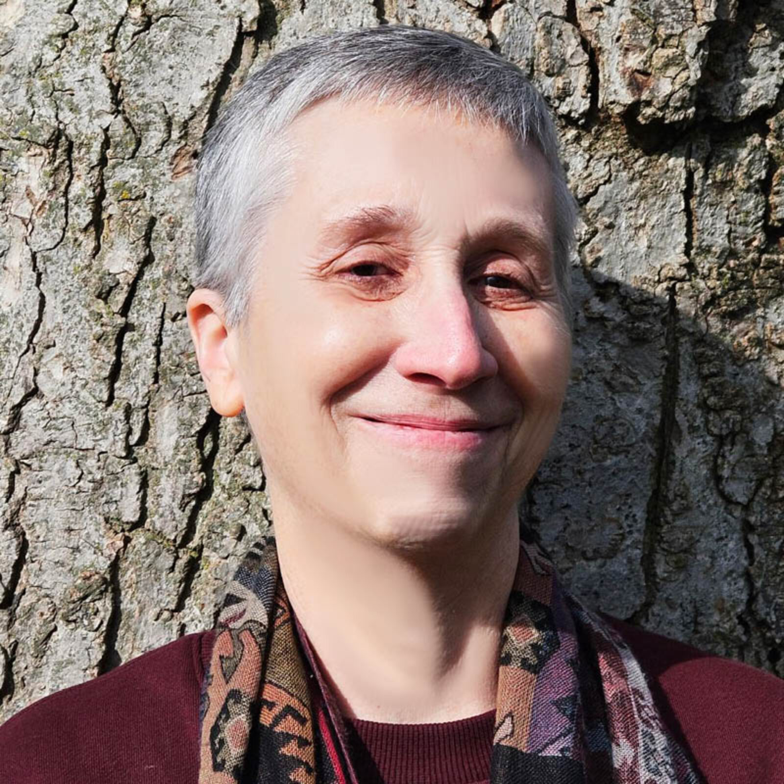 woman smiling in front of a tree with burgandy shirt and colorful scarf