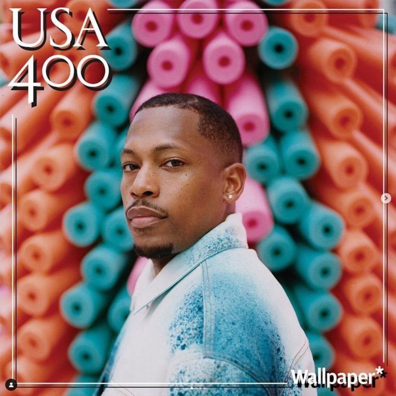 man standing body facing left head turned towards camera with foam rollers behind him multicolored