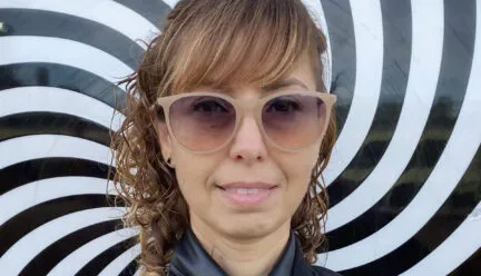 blond woman with sunglasses smiling at camera with straight and curly hair blue zipped up rain jacket and blakc and white rotating background