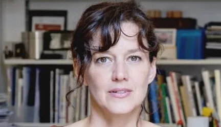 woman with light complexion looking at camera, black curly hair, pinkish shirt