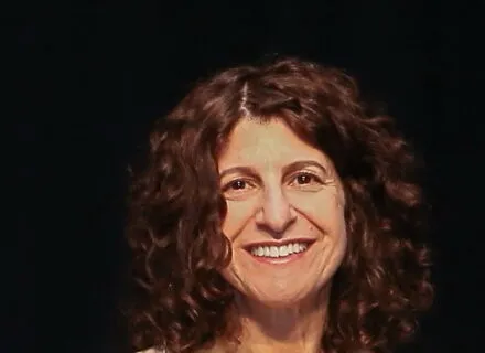 olive complexion female with curly brunette hair outlining face smiling wearing beige blaver and olive colored top