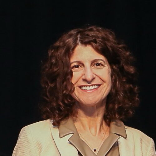 olive complexion female with curly brunette hair outlining face smiling wearing beige blaver and olive colored top