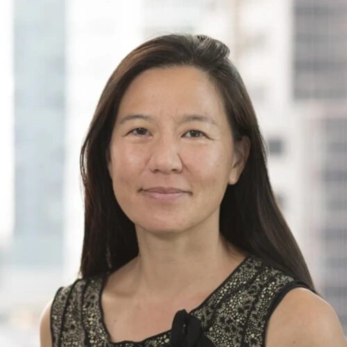 olive complexion with long black hair, smiling mouth closed at camera, wearing patterned top